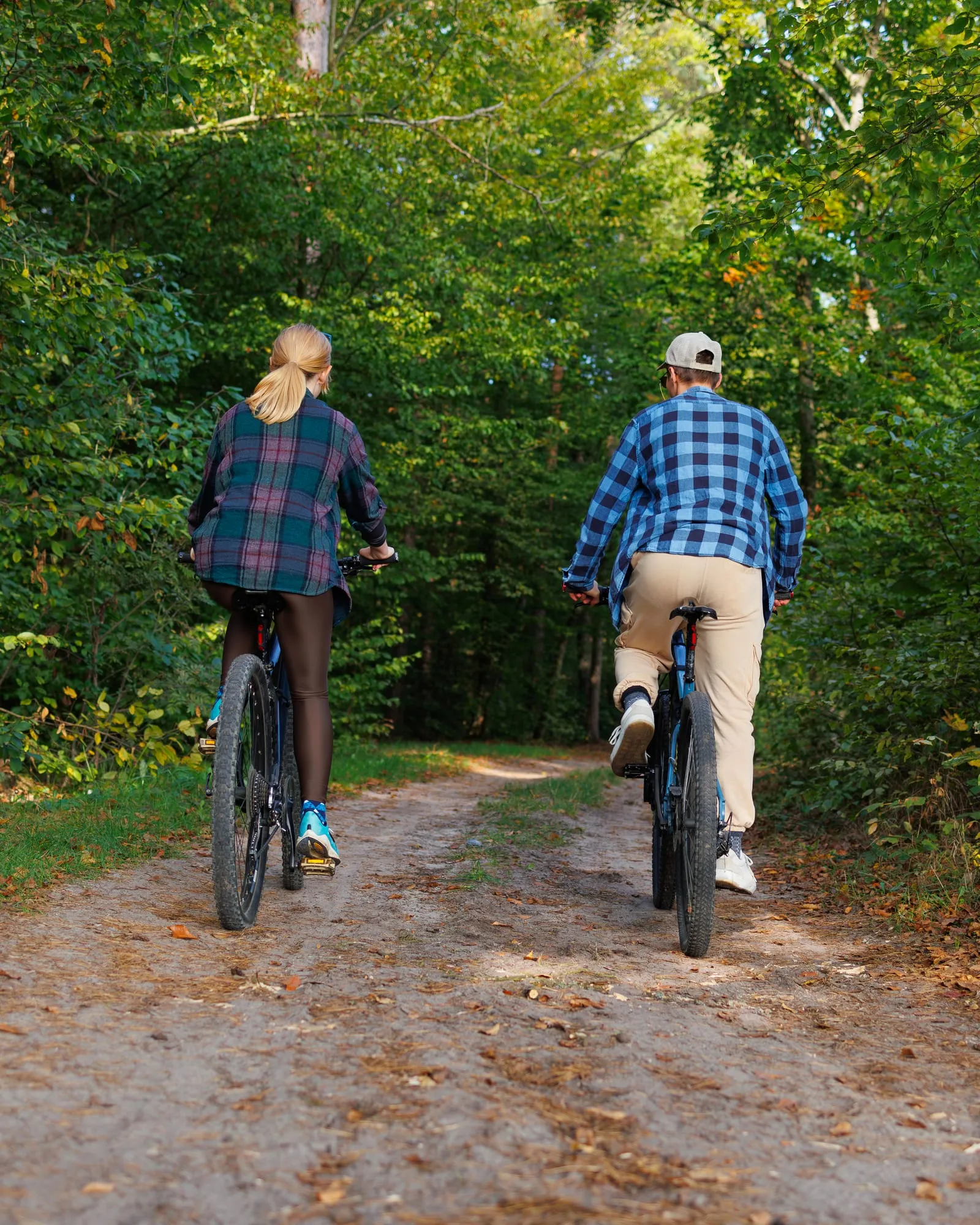 Two cyclists riding away along a sunlit woodland trail.